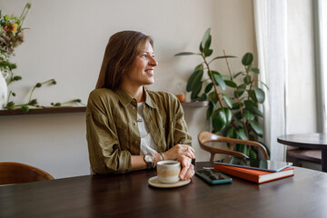 A woman smiles while sipping coffee in a cozy caf surrounded by plants