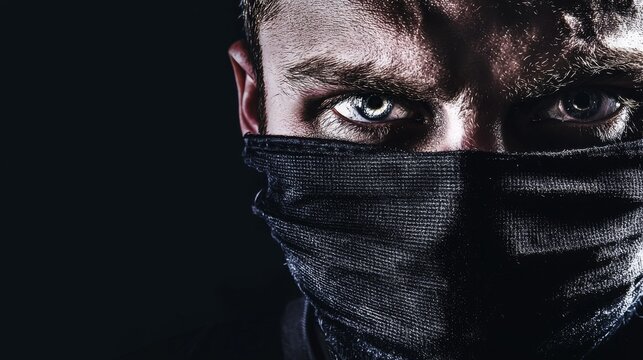 Close-up of a man's intense eyes peering out from behind a dark mask, creating a mysterious and brooding atmosphere. - Powered by Adobe