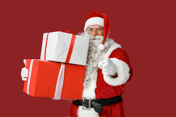 Santa Claus with Christmas gifts pointing at viewer on red background