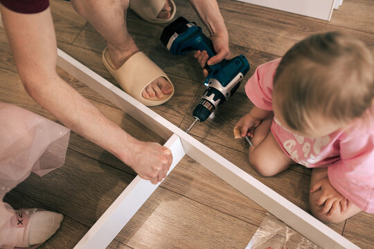 Father and daughters assemble a new bed using a screwdriver.