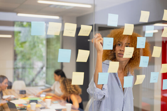 Focused coworker writing on sticky notes on office glass wall