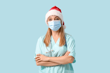 Mature female doctor in Santa hat and medical mask on blue background