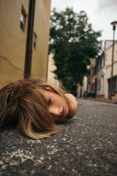 Mannequin head with hair lying on the street near a sidewalk.