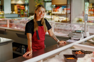 A cheerful fishmonger proudly stands at a seafood counter, showcasing a variety of fresh seafood...