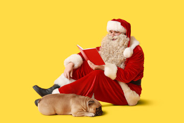 Santa Claus with cute French bulldog reading book on yellow background