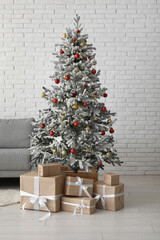 Beautiful Christmas tree with sofa and gift boxes near white brick wall