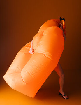 Playful Figure Embraces Large Inflatable Orange Object Indoors