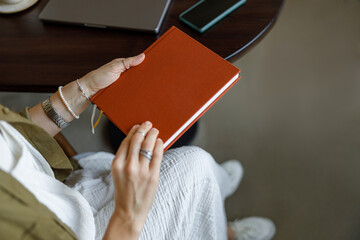 A person is holding an orange notebook, which beautifully showcases a calm and creative workspace environment