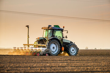 Green tractor seeding soil with planter in agricultural field during golden hour