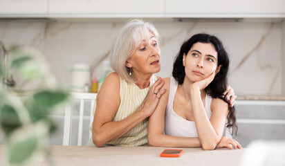 Elderly mother asks for forgiveness from her adult daughter and calms her down after a domestic quarrel in the kitchen