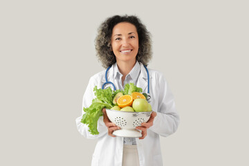 Mature female nutritionist with healthy food on light background