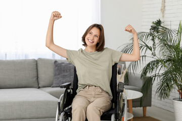 Young pretty woman in wheelchair showing strength gesture at home