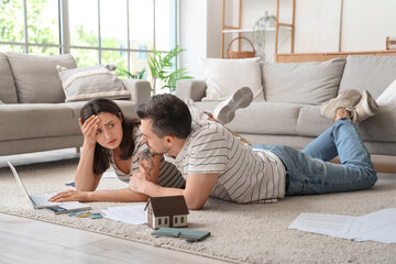 Young couple lying on floor with laptop and discussing debt at home. Bankruptcy concept