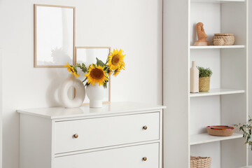 Vase of sunflowers bouquet with frames on commode in living room