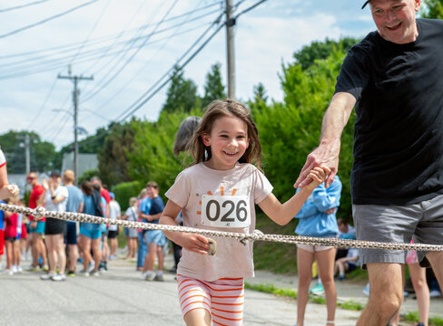 Child and her father run across the finish line at a running race even