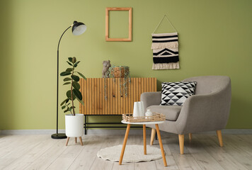 Interior of modern room with comfortable armchair, coffee table and commode near green wall