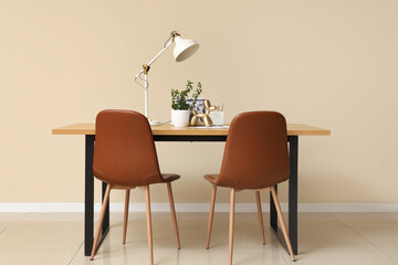 Wooden table with houseplant, figurine, magazines and desk lamp near beige wall