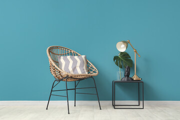 Chair and coffee table with figurine, monstera leaf and desk lamp near blue wall