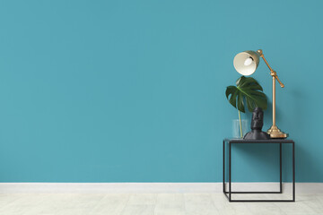 Coffee table with figurine, monstera leaf and desk lamp near blue wall