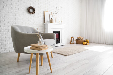 Interior of stylish room with modern fireplace, armchair and autumn decorations near white brick wall