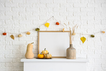 Naklejka premium Frame with pumpkins, vase and autumn garland on modern fireplace near white brick wall