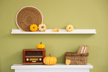 Naklejka premium Vintage radio receiver with pumpkins and books on modern fireplace near green wall