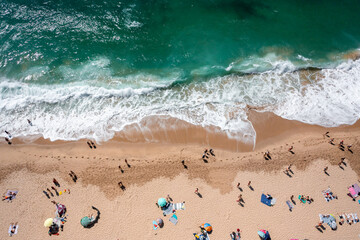 Overhead drone shot of anonymous tourist and colorful parasols on sandy seashore. From above of...