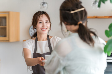 キッチン・カウンターからコーヒーカップを手渡すエプロン姿のカフェ店員のアジア人女性  © buritora