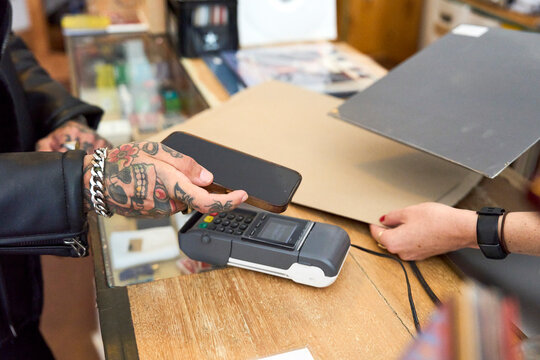 Customer making a contactless payment with phone in a record store