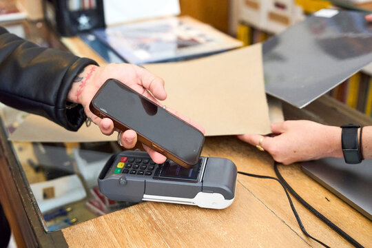 Customer making a contactless payment with phone in a record store