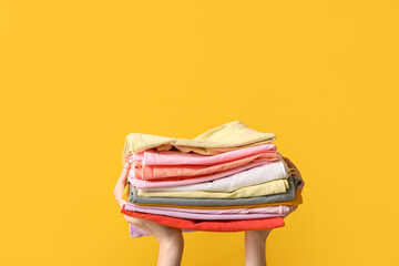 Female hands with stack of different clothes on yellow background