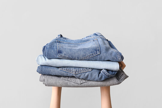 Female hands with stack of different jeans on grey background