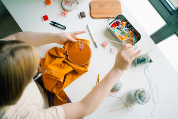 Person hand stitching a floral embroidery pattern on orange fabric

