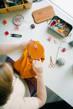 Person hand embroidering a floral design with colorful threads

