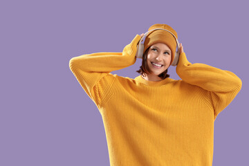 Young woman in yellow sweater with headphones on lilac background