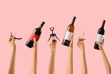 Female hands holding bottles of wine and corkscrews on pink background
