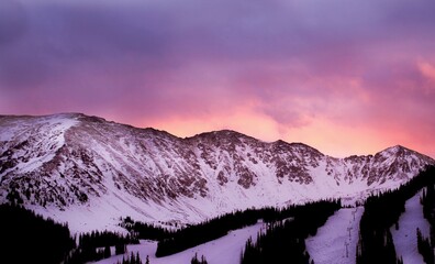 A vibrant winter sunset paints the snowy mountains in shades of pink and purple. 