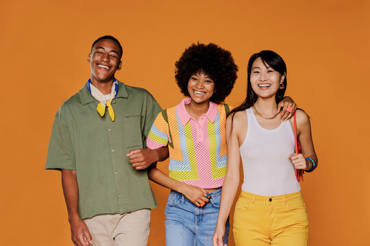 Three friends walking and smiling on orange background