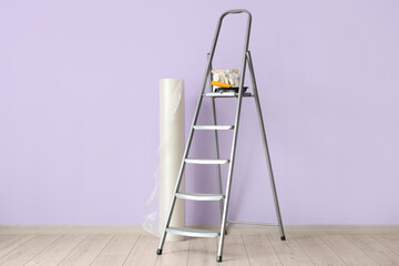 Stepladder with roll of bubble wrap, cans of paint and tools near lilac wall