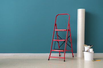 Stepladder with roll of bubble wrap, cans of paint and brushes near blue wall