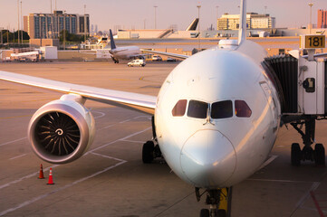 Cockpit of a modern jet airplane on tarmac of the airport lit with sunset sun rays. Close-up with widows of the crew cabin and jet engine suspended on the plane's wing