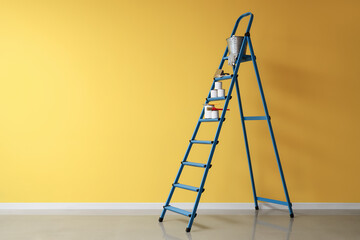 Stepladder with cans of paint and brushes near yellow wall