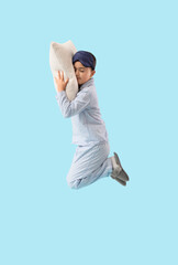 Cute little boy in pajamas with pillow jumping on blue background