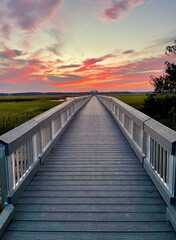 A long boardwalk stretches into a vibrant sunset over the marshlands in Charleston, with colorful clouds illuminating the sky.