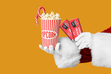 Santa's hands with bucket of popcorn, cinema tickets and candy canes on yellow background