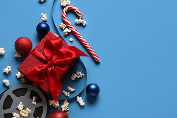 Scattered popcorn, film reel, gift box and Christmas decor on blue background