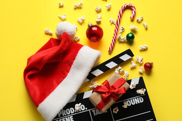 Scattered popcorn, movie clapper, gift box and Christmas decor on yellow background