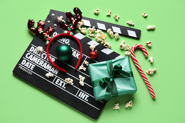 Scattered popcorn, movie clapper, gift box and Christmas decor on green background