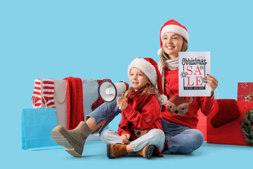 Obraz premium Beautiful young woman holding paper with text CHRISTMAS SALE and her cute little daughter with megaphone on blue background