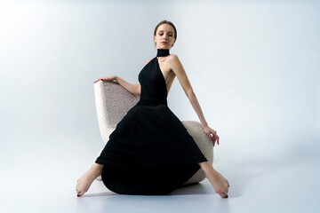 young woman in a long black evening dress is sitting on an armchair, style and self-confidence